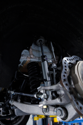 Close-up of a vehicle's undercarriage showing the suspension system with a shock absorber, coil spring, brake rotor, and control arms.
